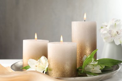 Photo of Burning candles and beautiful flowers on white table. Space for text