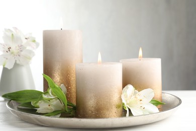 Photo of Burning candles and beautiful flowers on white table