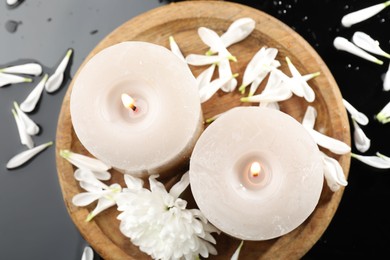 Photo of Burning candles and beautiful flowers on black table, flat lay