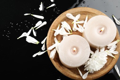 Photo of Burning candles and beautiful flowers on black table, flat lay