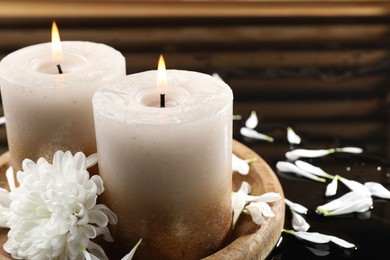 Photo of Burning candles and beautiful flowers on wet black mirror surface, closeup