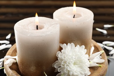 Photo of Burning candles and beautiful flowers on wet black mirror surface, closeup