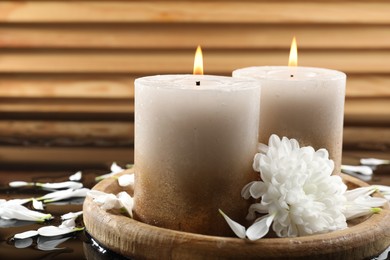 Photo of Burning candles and beautiful flowers on wet black mirror surface, closeup
