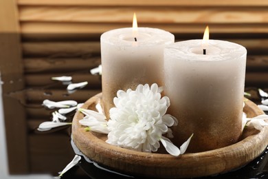 Photo of Burning candles and beautiful flowers on wet black mirror surface, closeup