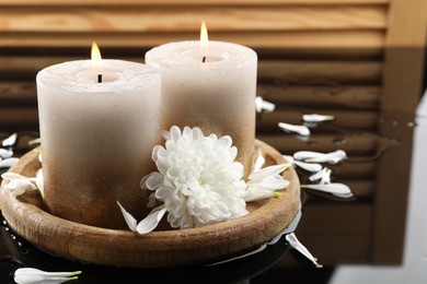 Photo of Burning candles and beautiful flowers on wet black mirror surface, closeup
