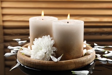 Photo of Burning candles and beautiful flowers on wet black mirror surface, closeup