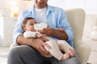 Photo of Father feeding his little baby with bottle on armchair at home, closeup