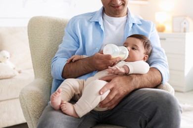 Photo of Father feeding his little baby with bottle on armchair at home, closeup