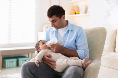 Photo of Father feeding his little baby with bottle on armchair at home