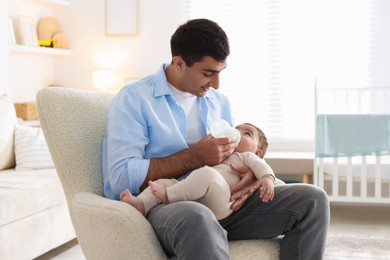 Photo of Father feeding his little baby with bottle on armchair at home
