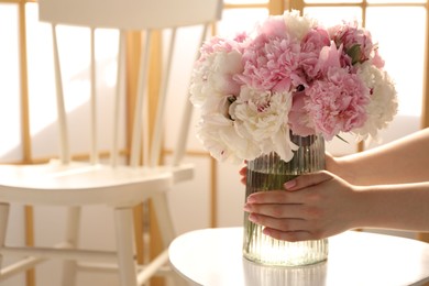 Photo of Woman putting beautiful peonies into vase at white table indoors, closeup. Space for text