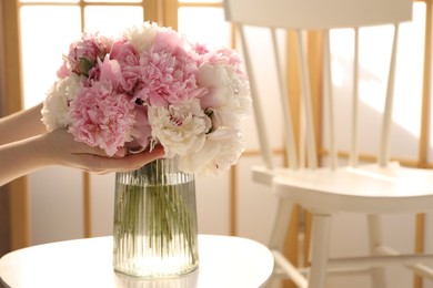 Photo of Woman putting beautiful peonies into vase at white table indoors, closeup. Space for text