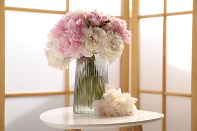 Photo of Beautiful peonies in vase on white table indoors