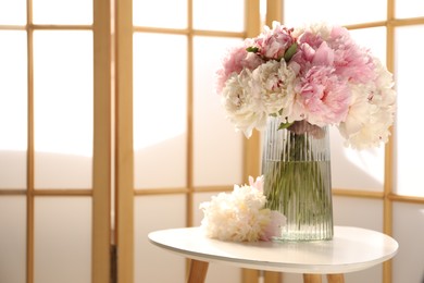 Photo of Beautiful peonies in vase on white table indoors, space for text