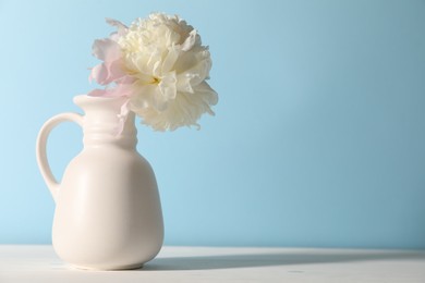 Photo of Beautiful peony in vase on white table near light blue wall. Space for text