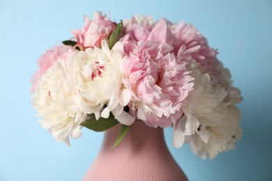 Photo of Beautiful peonies in vase on light blue background, closeup