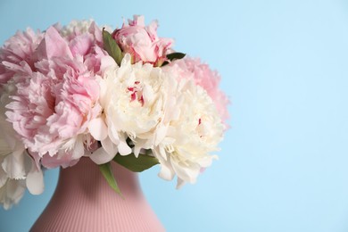 Photo of Beautiful peonies in vase on light blue background, closeup. Space for text