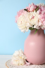 Photo of Beautiful peonies in vase on white table near light blue wall, closeup