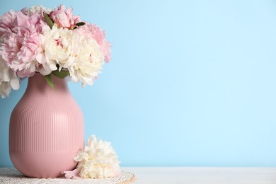 Photo of Beautiful peonies in vase on white table near light blue wall. Space for text