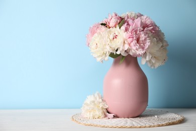 Photo of Beautiful peonies in vase on white table near light blue wall. Space for text