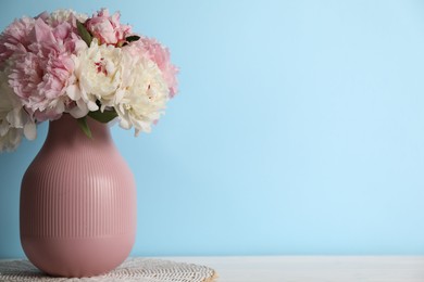 Photo of Beautiful peonies in vase on white table near light blue wall. Space for text