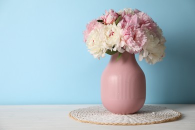 Photo of Beautiful peonies in vase on white table near light blue wall. Space for text