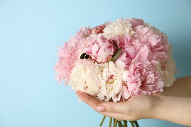 Photo of Woman holding bouquet of beautiful peonies on light blue background. Space for text