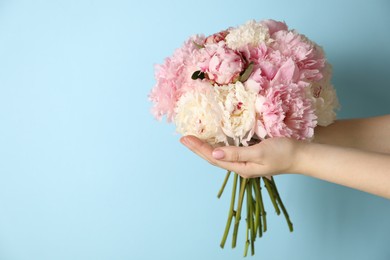 Photo of Woman holding bouquet of beautiful peonies on light blue background. Space for text