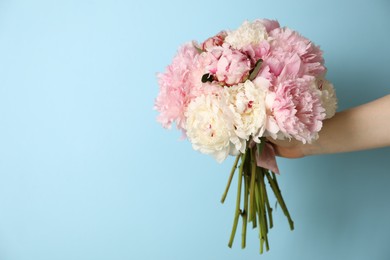 Photo of Woman holding bouquet of beautiful peonies on light blue background. Space for text