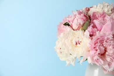 Photo of Beautiful peonies in vase on light blue background, closeup. Space for text