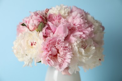 Photo of Beautiful peonies in vase on light blue background, closeup