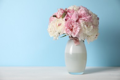 Photo of Beautiful peonies in vase on white table near light blue wall. Space for text
