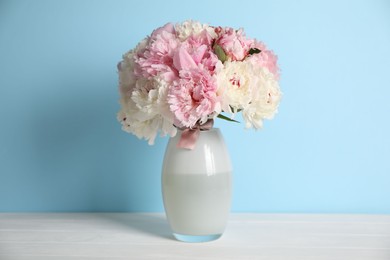 Photo of Beautiful peonies in vase on white table near light blue wall