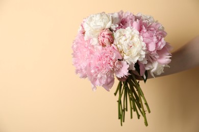 Photo of Woman holding bouquet of beautiful peonies on beige background, closeup. Space for text