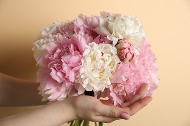 Photo of Woman holding bouquet of beautiful peonies on beige background, closeup