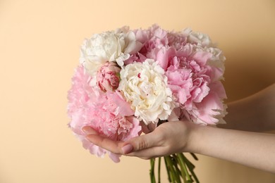 Photo of Woman holding bouquet of beautiful peonies on beige background, closeup