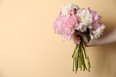 Photo of Woman holding bouquet of beautiful peonies on beige background, closeup. Space for text