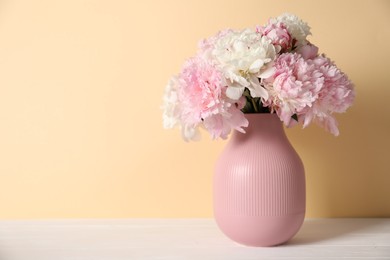 Photo of Beautiful peonies in vase on white table against beige background. Space for text