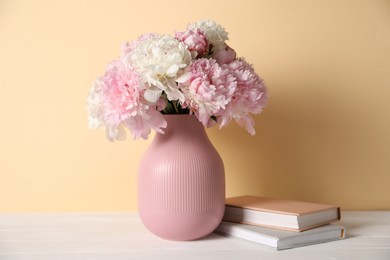 Photo of Beautiful peonies in vase and books on white table against beige background