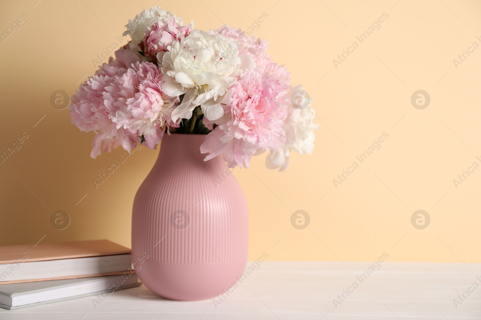 Beautiful peonies in vase and books on white table against beige background. Space for text Photo of Beautiful peonies in vase and books on white table against beige background. Space for text