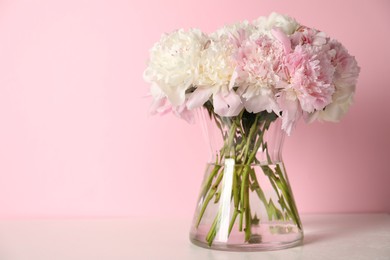 Photo of Beautiful peonies in vase on white table against pink background. Space for text