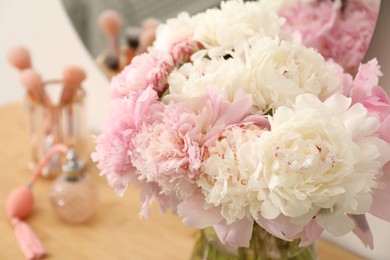 Photo of Beautiful peonies in vase and mirror on wooden vanity indoors, closeup