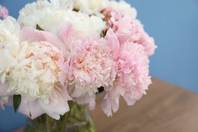 Photo of Beautiful peonies in vase on wooden table near light blue wall, closeup