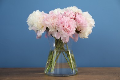 Photo of Beautiful peonies in vase on wooden table near light blue wall