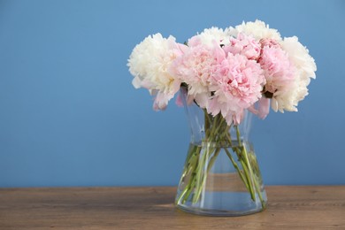 Photo of Beautiful peonies in vase on wooden table near light blue wall. Space for text