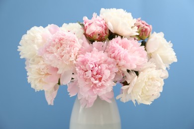 Photo of Beautiful peonies in vase on light blue background, closeup
