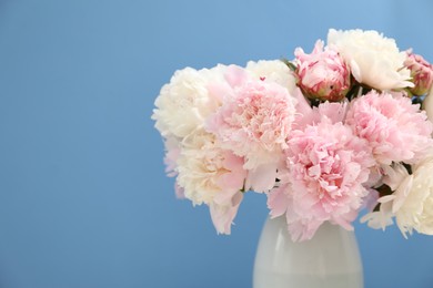 Photo of Beautiful peonies in vase on light blue background, closeup. Space for text