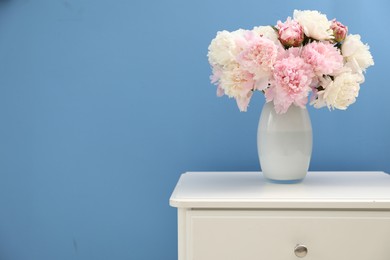Photo of Beautiful peonies in vase on white dresser near light blue wall. Space for text