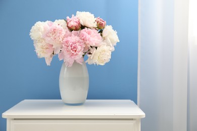 Photo of Beautiful peonies in vase on white dresser near light blue wall. Space for text