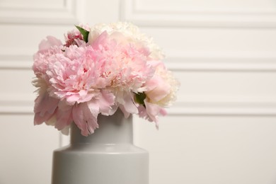 Photo of Beautiful peonies in vase near white wall, closeup. Space for text